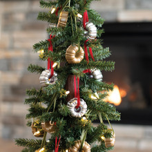 Two golden cast aluminum Nordic Ware bundt-shaped ornaments hanging on Christmas tree near glowing fireplace