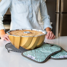 Nordic Ware silicone bundt-shaped hot pads in front of golden baked bundt cake with fluted design