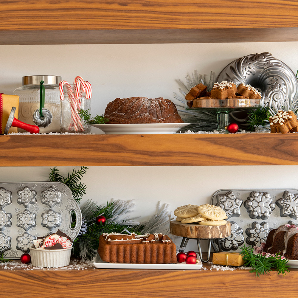 Three decorated bundt cakes on white shelves with holiday ornaments and pine garland, showcasing winter baking