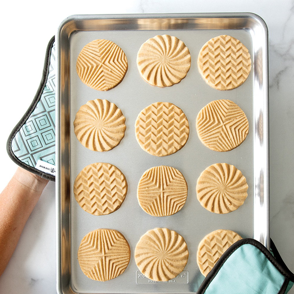 Two Nordic Ware bundt-shaped hot pads holding aluminum half sheet pan with golden baked cookies
