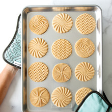Two Nordic Ware bundt-shaped hot pads holding aluminum half sheet pan with golden baked cookies