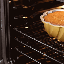 Person using Nordic Ware bundt-shaped silicone hot pads to safely remove golden bundt cake from oven