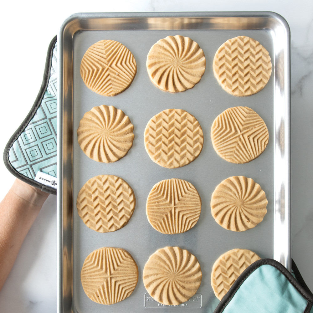 Two Nordic Ware bundt-shaped hot pads holding aluminum half sheet pan with golden baked cookies
