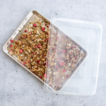 Nordic Ware aluminum half sheet pan with clear lid, containing golden baked granola clusters