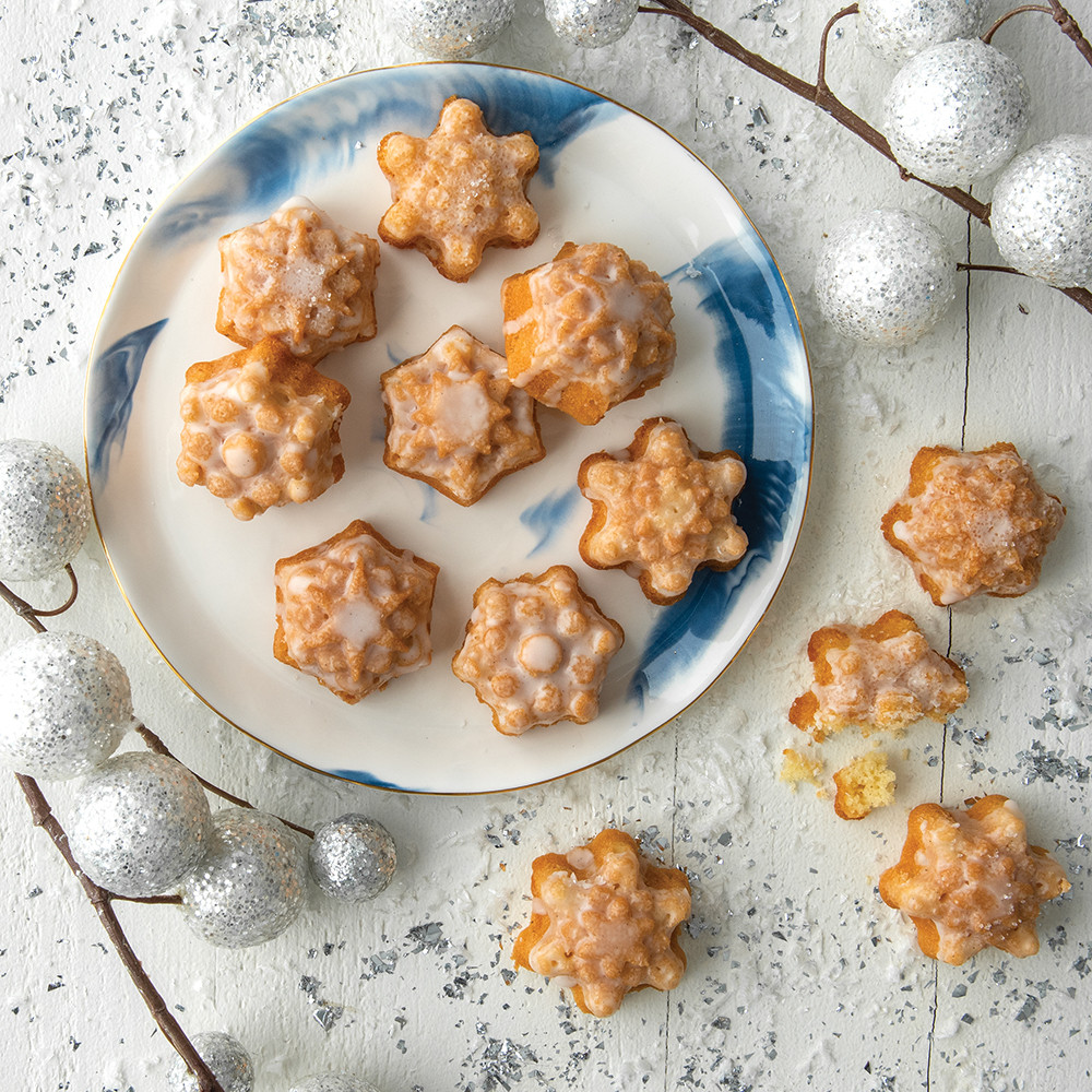 Golden snowflake-shaped cake bites arranged on white plate with decorative snow, baked in Nordic Ware pan
