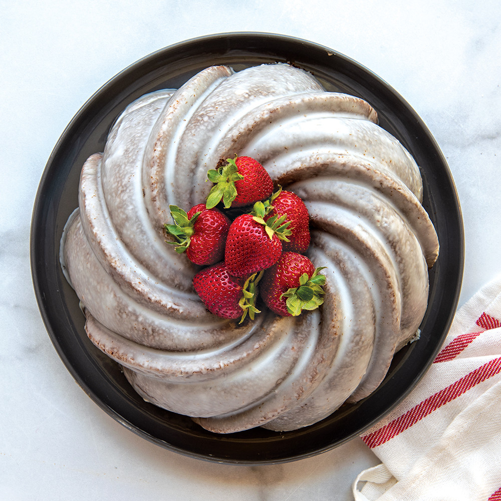 Golden swirl bundt cake with white glaze and fresh strawberries, baked in Nordic Ware aluminum bundt pan