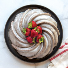 Golden swirl bundt cake with white glaze and fresh strawberries, baked in Nordic Ware aluminum bundt pan