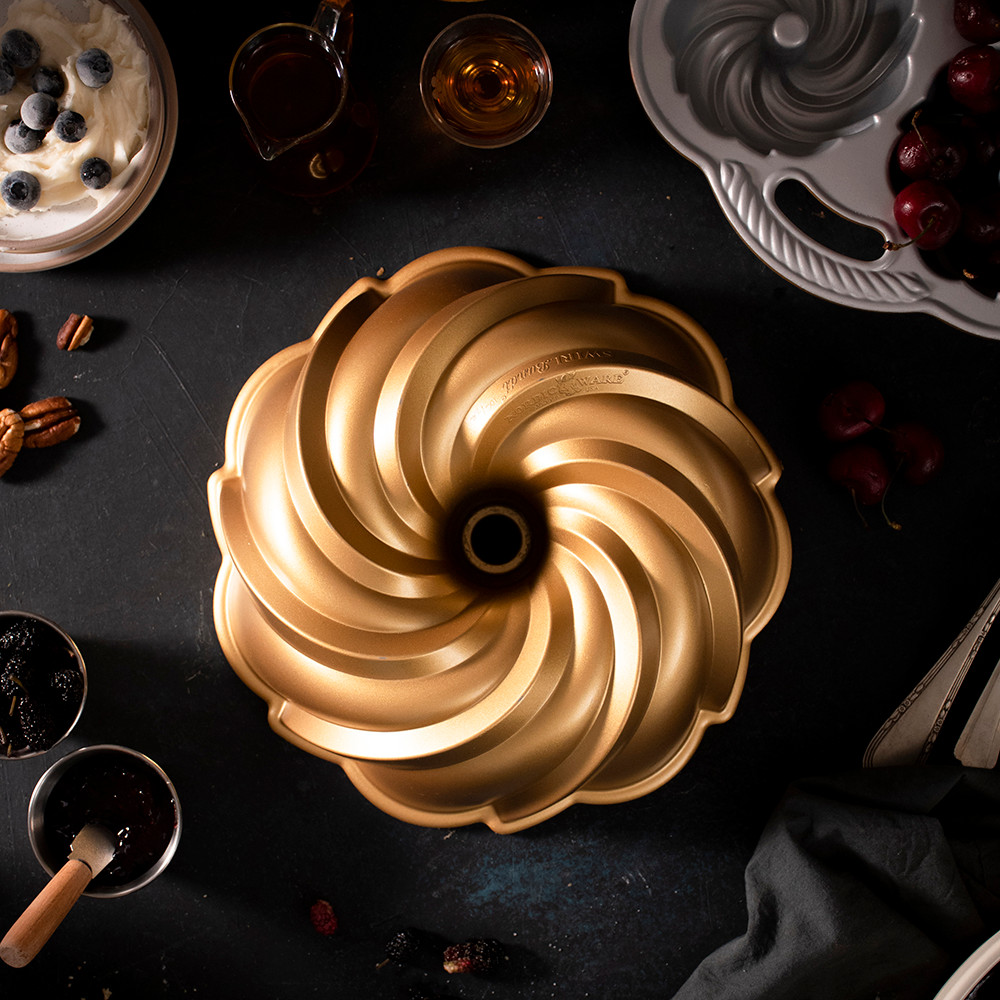 Nordic Ware aluminum Swirl Bundt pan with spiral fluted design, natural silver finish, shown with baking ingredients