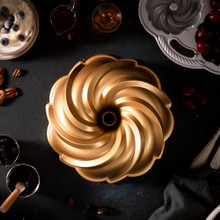 Nordic Ware aluminum Swirl Bundt pan with spiral fluted design, natural silver finish, shown with baking ingredients