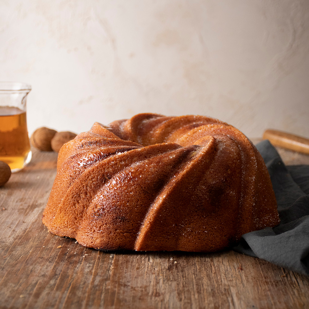 Golden bundt cake with swirled ridged pattern baked in Nordic Ware aluminum pan, baking ingredients visible