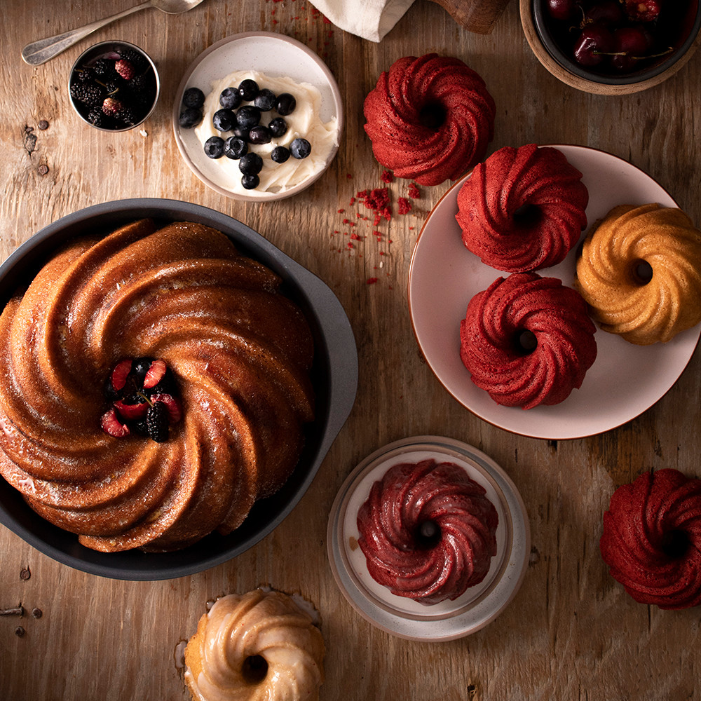 Four bundt cakes with decorative swirl patterns baked in Nordic Ware aluminum bundt pans, overhead view