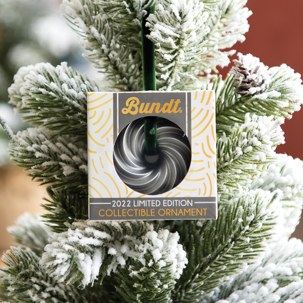 Nordic Ware Heritage Bundt ornament in packaging hanging on Christmas tree branch with green needles