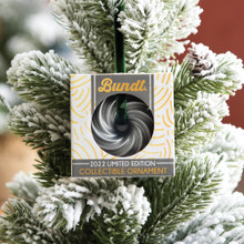 Nordic Ware Heritage Bundt ornament in packaging hanging on Christmas tree branch with green needles