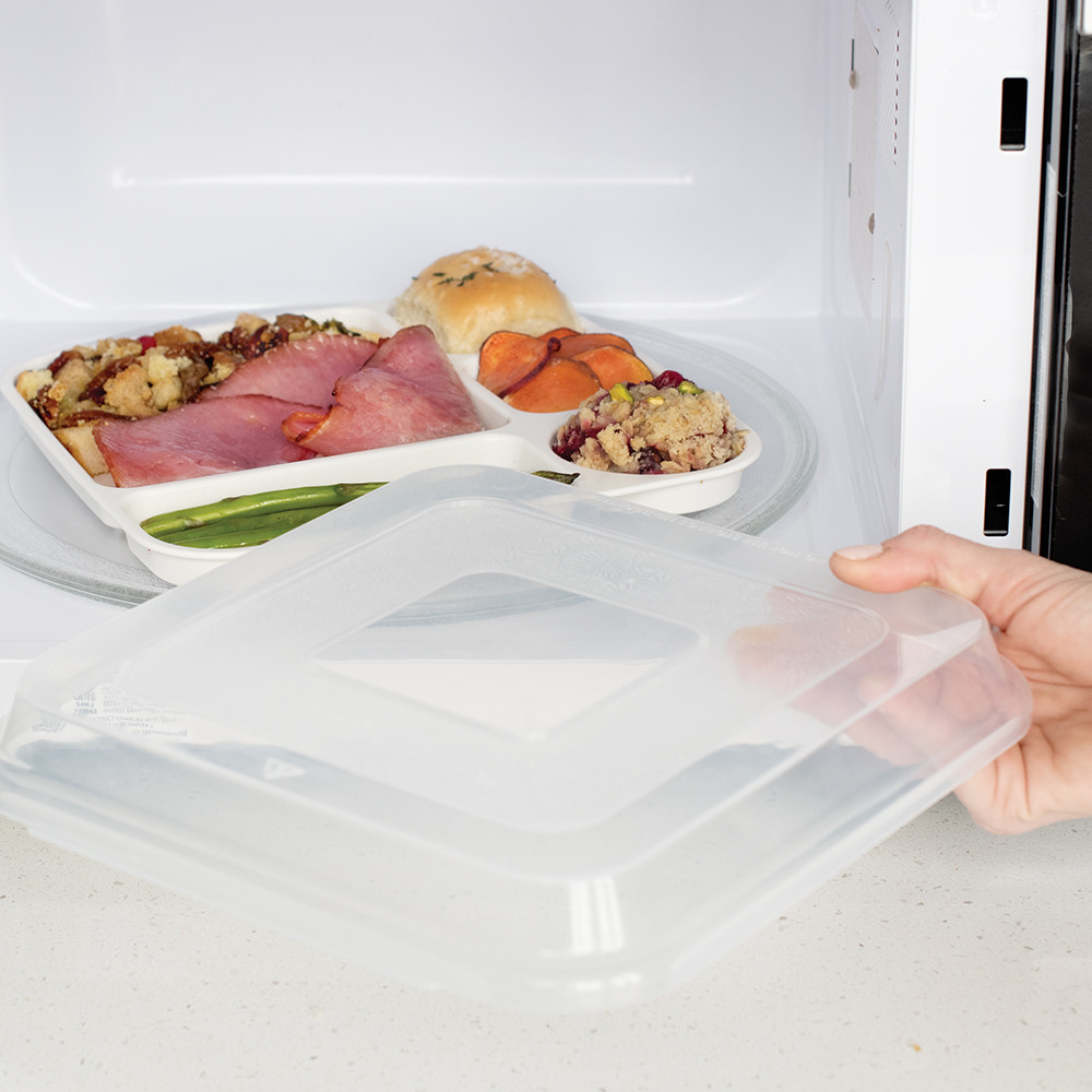 Gray Nordic Ware divided dinner tray with lid being reheated in microwave, containing cooked food portions