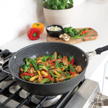 Nordic Ware Verde ceramic nonstick wok on stovetop with colorful stir-fried vegetables being cooked