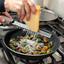 Basalt 10in Skillet lifestyle image with Brussel sprouts in pan, hand grating cheese into pan