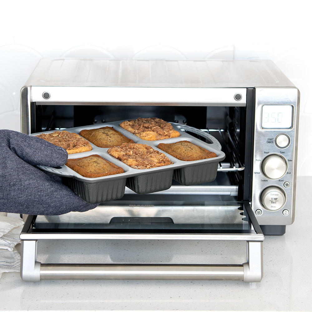Hand removing Nordic Ware ProCast aluminum mini loaf pan with golden baked bread from Breville toaster oven