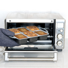 Hand removing Nordic Ware ProCast aluminum mini loaf pan with golden baked bread from Breville toaster oven