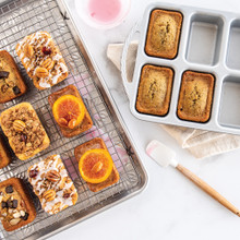 Six golden mini loaf cakes from Nordic Ware ProCast aluminum pan, being glazed with white icing and colorful toppings