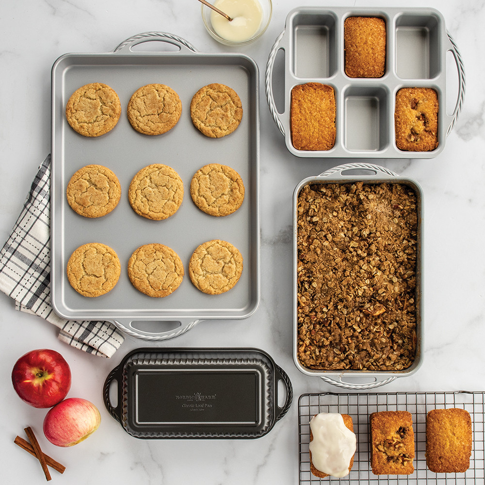 Nordic Ware ProCast aluminum baking pans with baked mini loaves, cookies, and apple crisp on marble surface