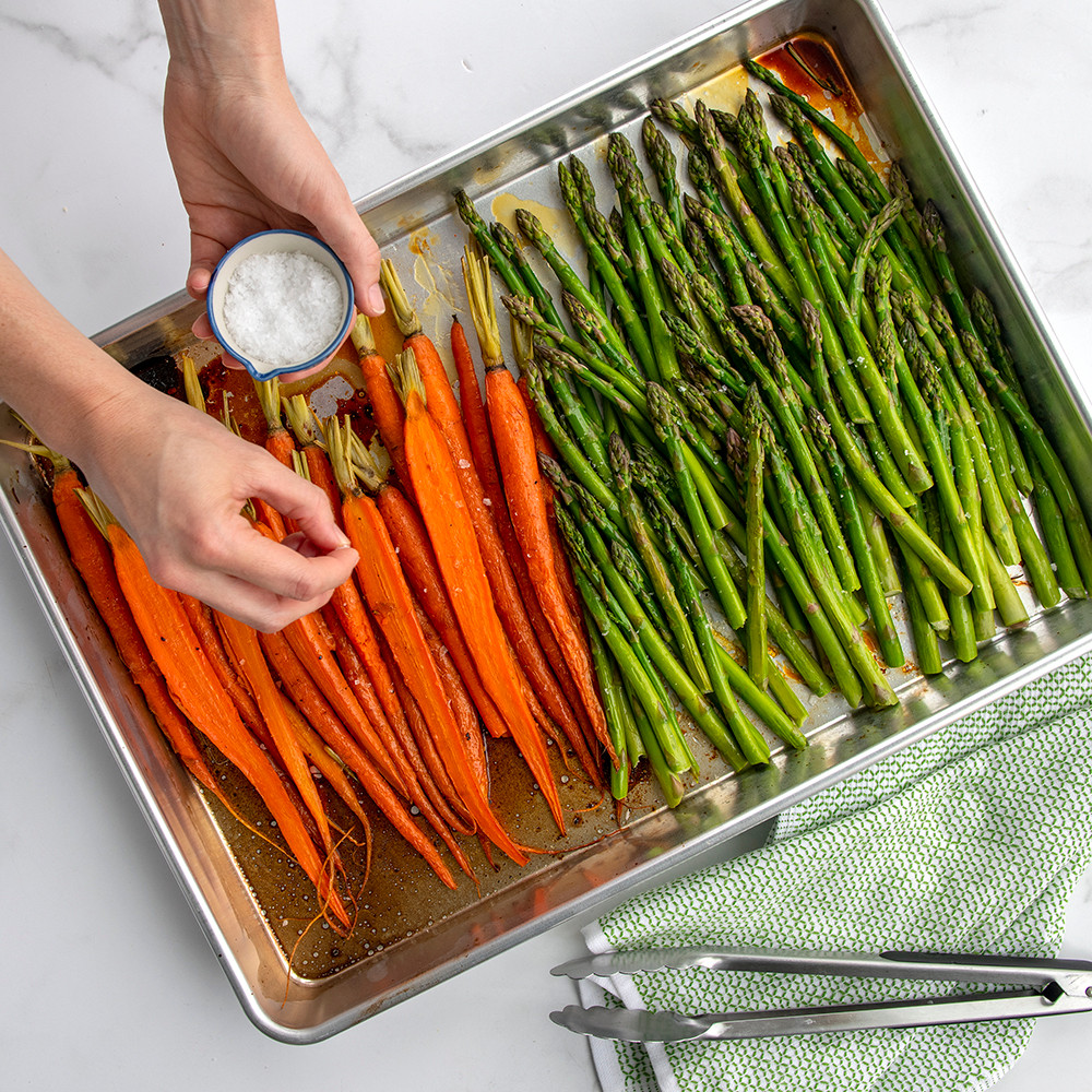 Nordic Ware aluminum Big Batch Pan with roasted mixed vegetables including carrots, onions, and peppers