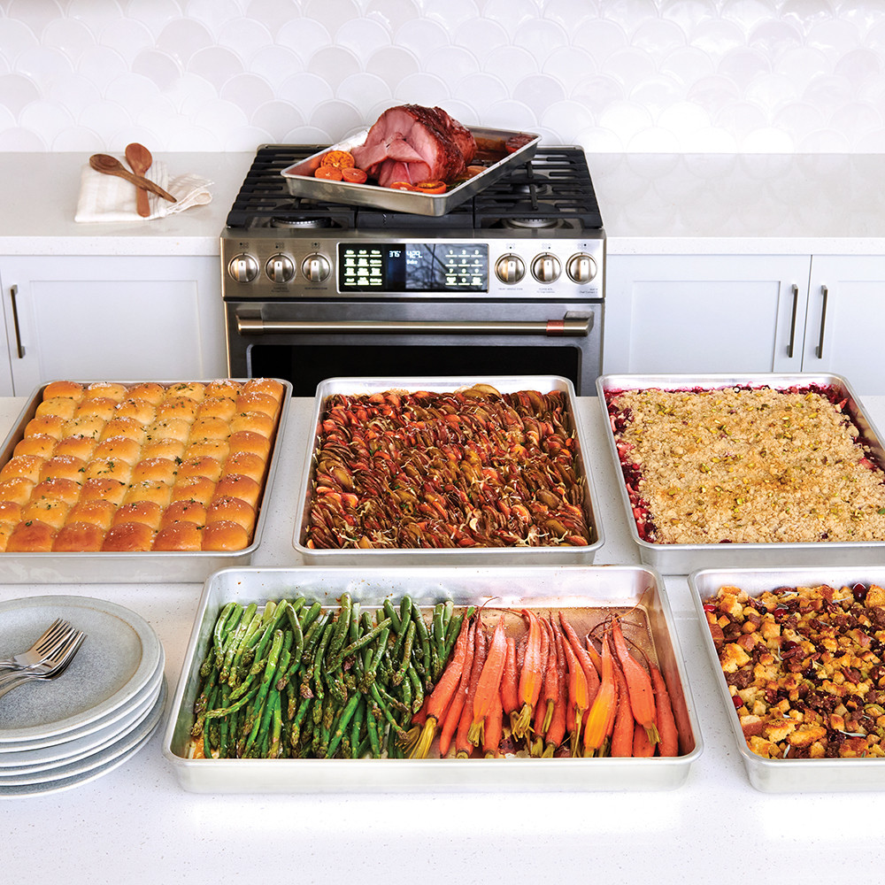 Two Nordic Ware aluminum Big Batch pans with baked lasagna and roasted vegetables on kitchen counter