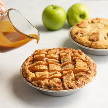 Hand drizzling caramel sauce over baked mini apple pies in Nordic Ware aluminum pie pans