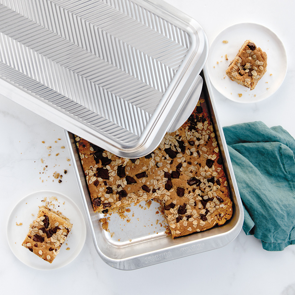 Nordic Ware rectangular aluminum baking pan with clear embossed prism lid containing golden chocolate chip cookie bars