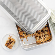 Chocolate chip cookie bars cut into squares in Nordic Ware 9x13 aluminum baking pan with prism-embossed lid