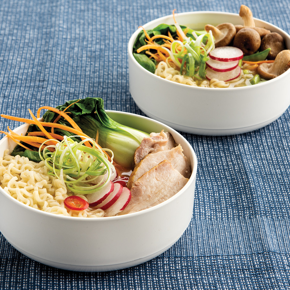 Two white ceramic Nordic Ware soup bowls filled with noodle soup containing vegetables and broth