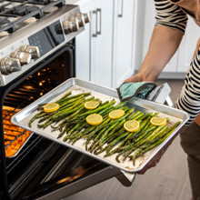 Hand removing Nordic Ware aluminum half sheet pan with roasted asparagus spears from oven, golden-brown tips