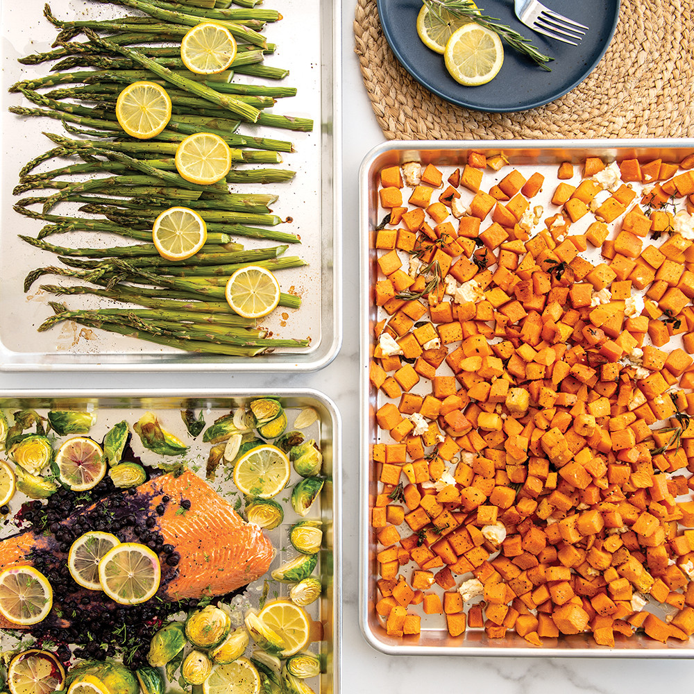 Three Nordic Ware aluminum sheet pans with roasted salmon, asparagus, and squash on marble countertop
