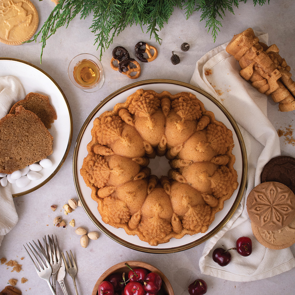 Golden bundt cake from Nordic Ware Very Merry pan with holly leaf design, decorated with fresh pine and red cherries