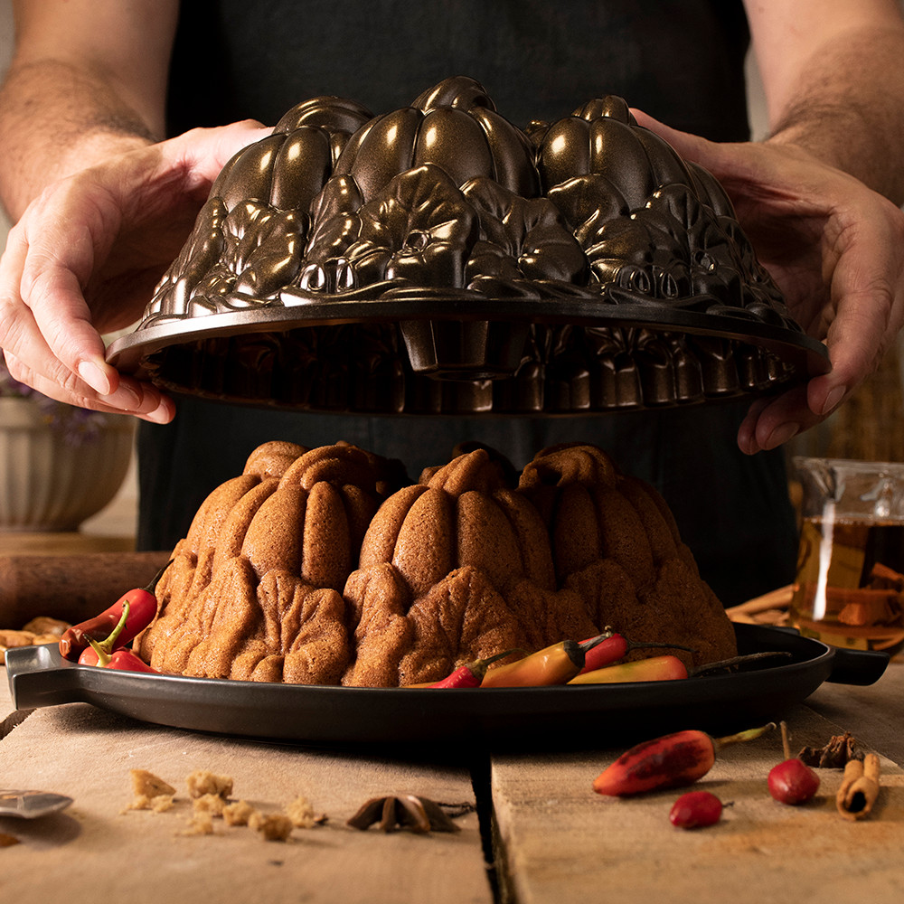 Person lifting golden pumpkin-shaped bundt cake from Nordic Ware aluminum Pumpkin Patch pan, revealing detailed ridged design