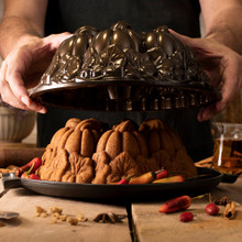 Person lifting golden pumpkin-shaped bundt cake from Nordic Ware aluminum Pumpkin Patch pan, revealing detailed ridged design