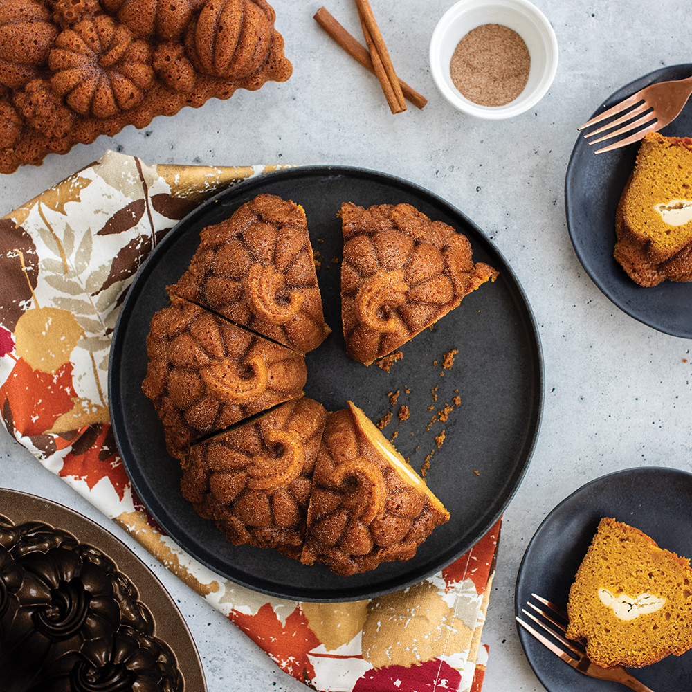 Sliced pumpkin-shaped bundt cake and rectangular loaf cake displayed with autumn decorations overhead view