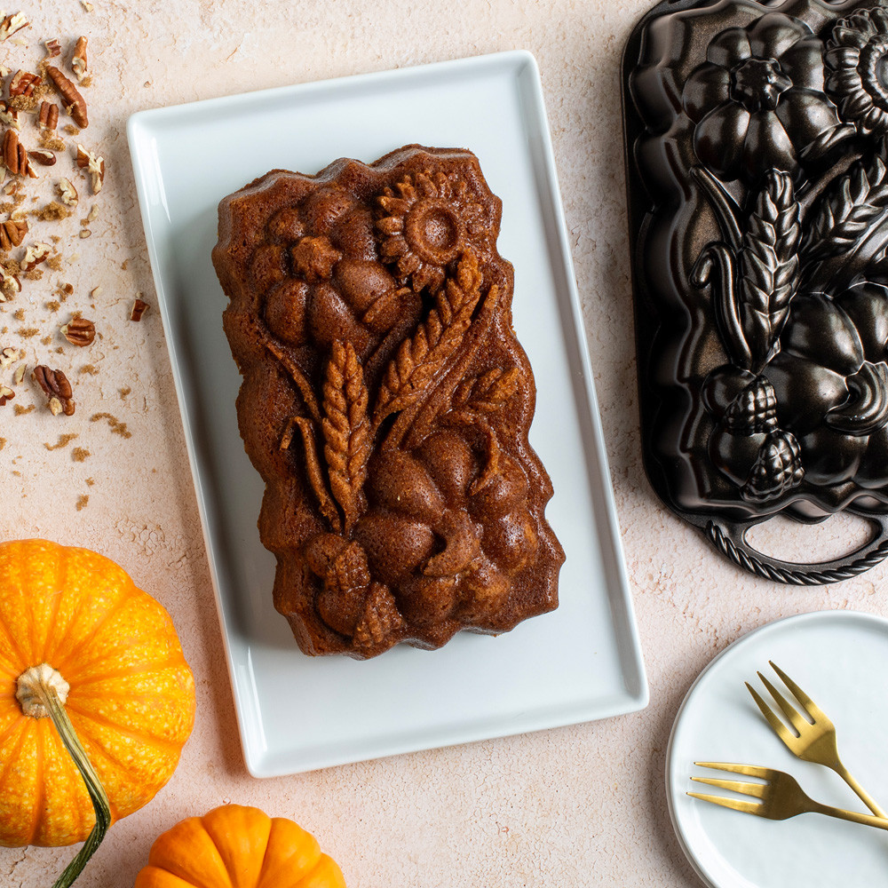 Overhead image of plain Sunflower Pumpkin Loaf cake on white plate surrounded pan, pumpkins and crushed pecans