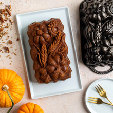 Overhead image of plain Sunflower Pumpkin Loaf cake on white plate surrounded pan, pumpkins and crushed pecans
