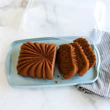 Sliced fluted loaf cake in clear Nordic Ware cake keeper with domed lid, showing golden brown interior