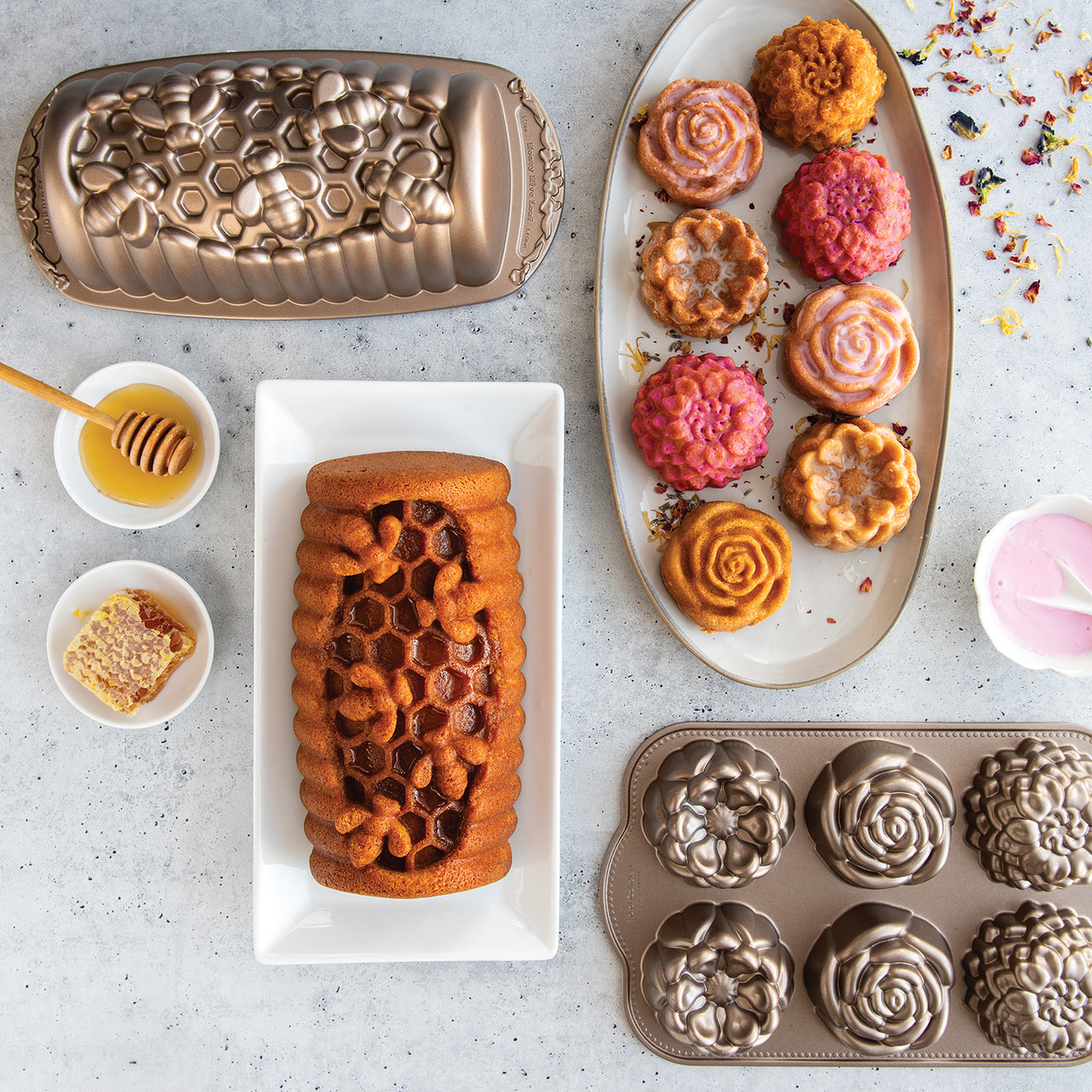 Six golden floral cakelets with white glaze on white plate, plus honey-glazed loaf cake from Nordic Ware pans