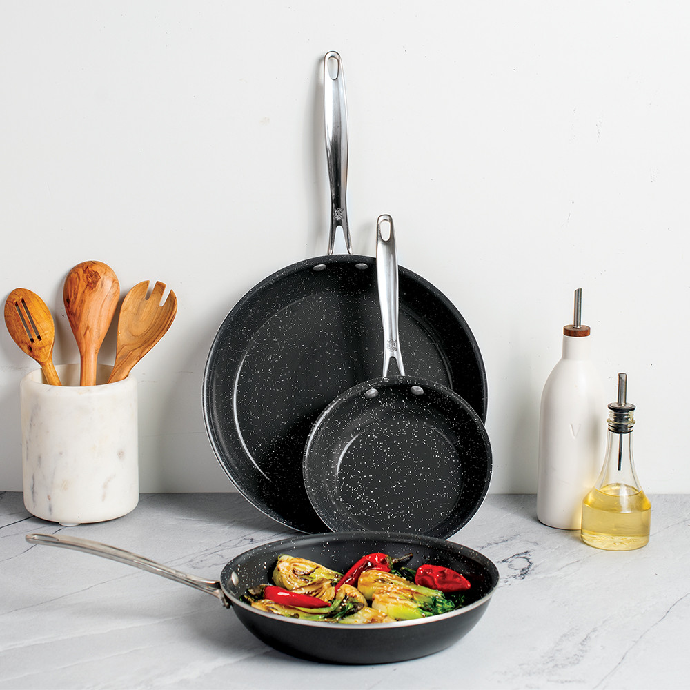 Three black non-stick skillets in graduated sizes from Nordic Ware Basalt collection displayed on white countertop