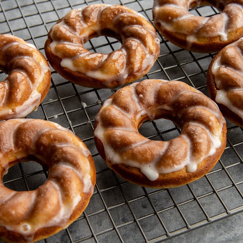 Six golden-brown French twist donuts with white glaze, baked in Nordic Ware aluminum donut pan on cooling rack