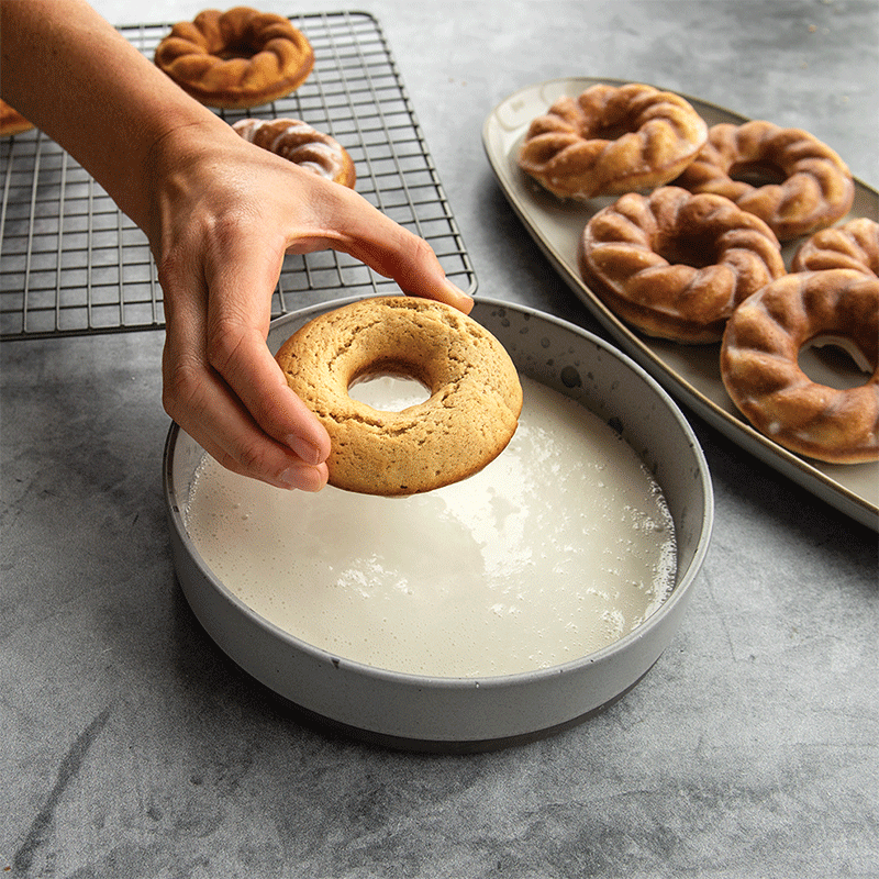 Hand dipping golden twisted donuts into white glaze, showing baking results from Nordic Ware French Twist pan