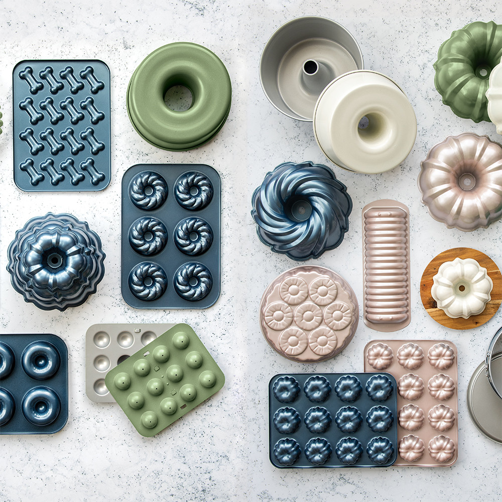 Collection of Nordic Ware aluminum baking pans in natural silver finish, including bundt, loaf, and specialty shaped molds