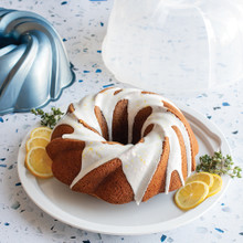 Nordic Ware aluminum swirl bundt pan with clear plastic cake keeper dome, silver finish with intricate spiral design