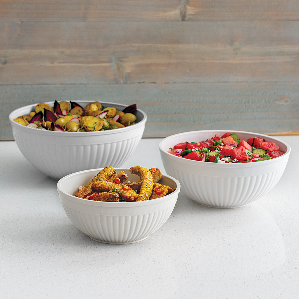 White Nordic Ware mixing bowls filled with fresh salad and fruit arranged on outdoor picnic table