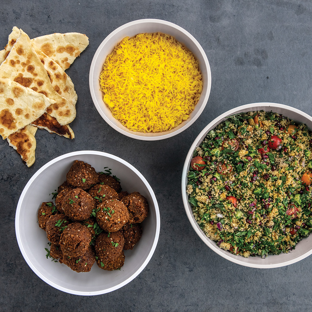 Three white ceramic mixing bowls with fresh ingredients: blueberries, herbs, and chopped vegetables arranged overhead
