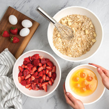 Nordic Ware 3 piece white prep and serve 5 quart, 3.5 quart and 2 quart bowls on kitchen countertop filled with strawberries, eggs and dough