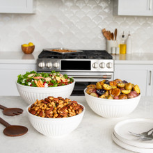 Nordic Ware 3 piece white prep and serve 5 quart, 3.5 quart and 2 quart bowls on kitchen countertop filled with salad, potatoes, and mixed nuts