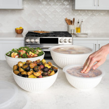 Nordic Ware 8 piece white bowl set including 7, 5, 3.5 and 2 quart bowls with lids on countertop; hand pushing lid onto a bowl  